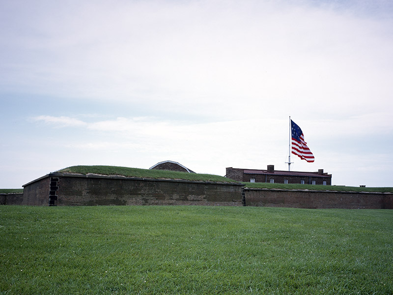 A large low stone fort on a grassy knoll with a US flag flying A large low stone fort on a grassy knoll with a US flag flying